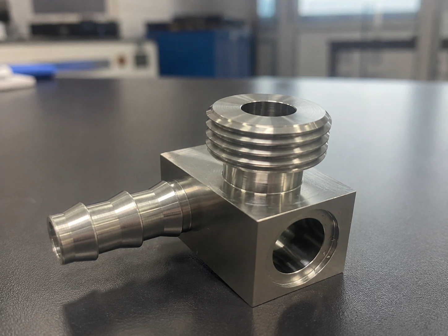 Machined stainless liquid cooling elbow fitting with a parallel male thread on a flat sealing shoulder, a multi-barb hose tail on the side and a bored port through the block