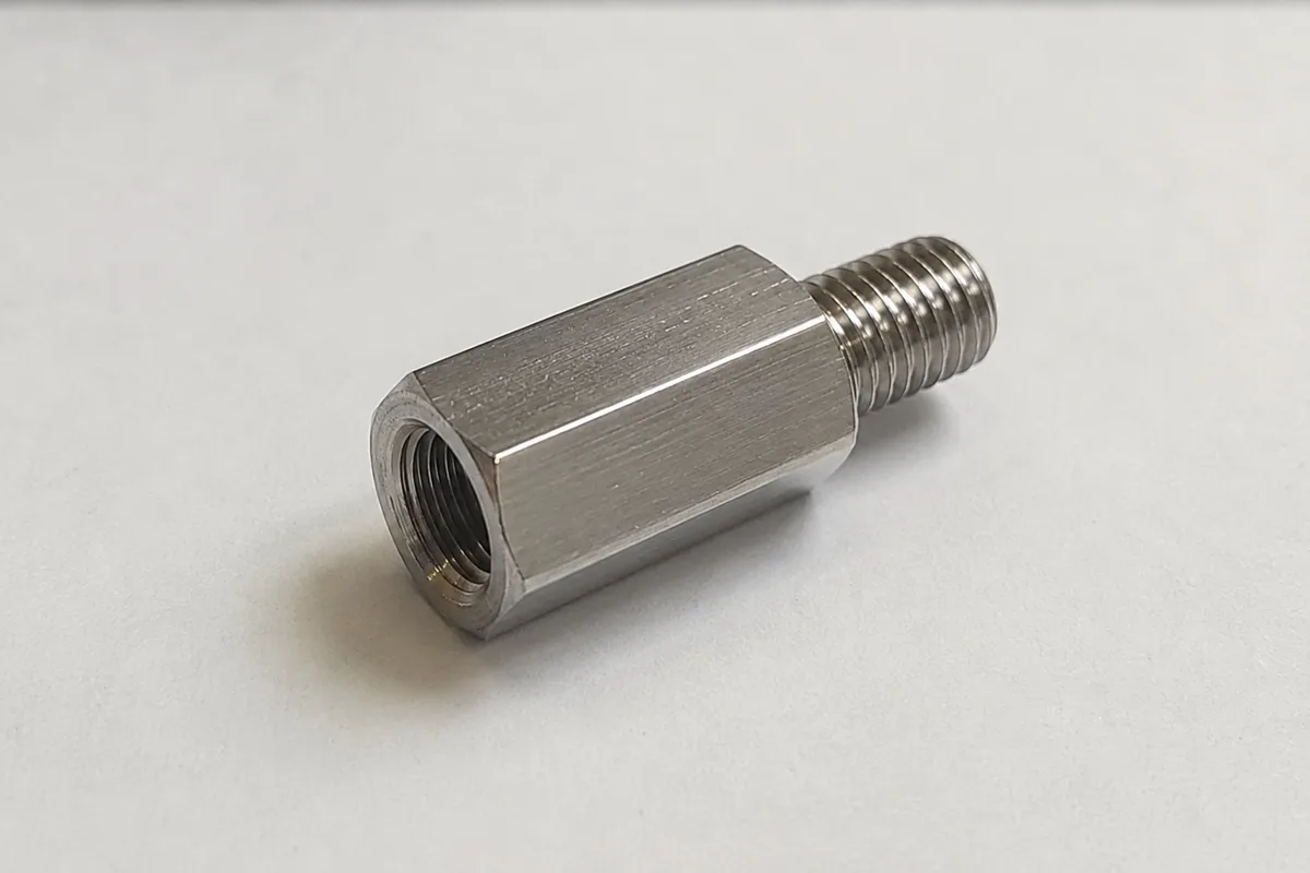 Machined stainless steel stepped thread reducer with male stud at one end and internal thread at the other on a light background
