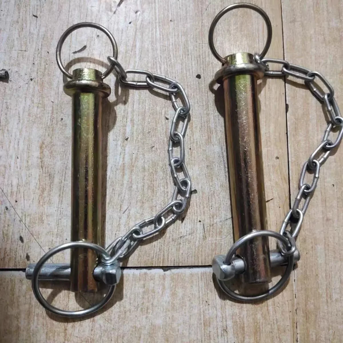 Two yellow zinc plated headed lock pins, each with a wire pull ring at the head, a linch pin through the cross hole at the nose, and a welded steel retaining chain running from the head ring to the linch pin