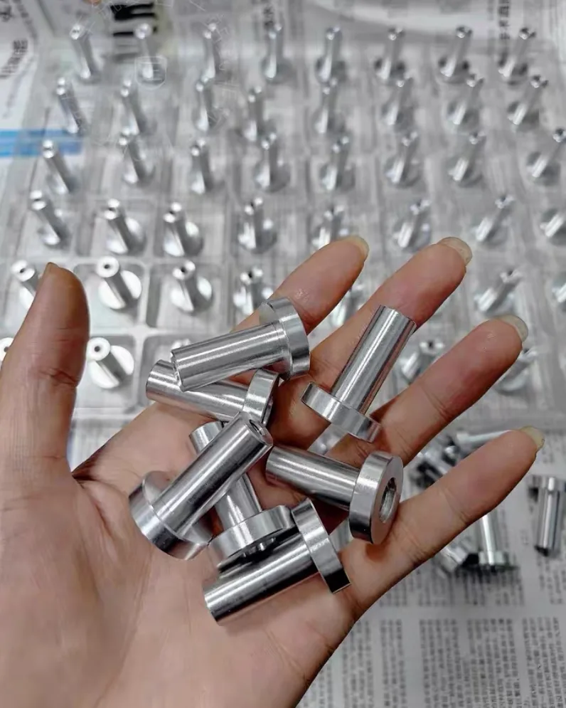 Hand holding a handful of turned aluminium flanged sleeves, more sleeves standing in a tray behind