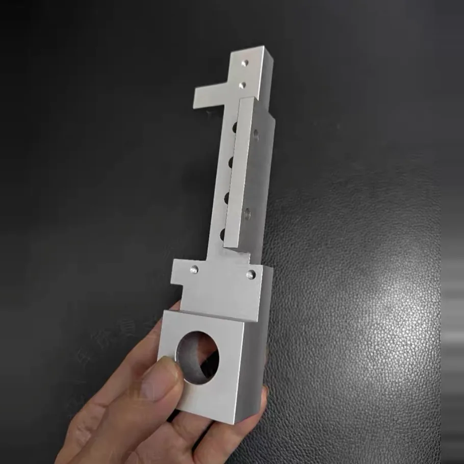 Hand holding an aluminium bracket with an upright rail, a row of holes and a bored block at the base