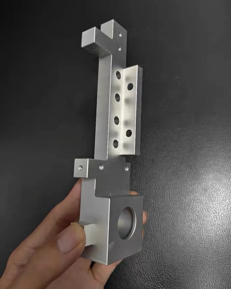 Hand holding an aluminium machine bracket with an angled rail carrying a hole row and a bored block at the base