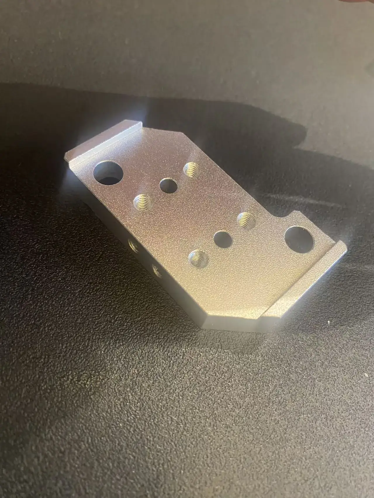 Angled view of the same aluminium mounting plate showing the raised lips on both short ends, the cut corners, the corner notch and the side tapped holes
