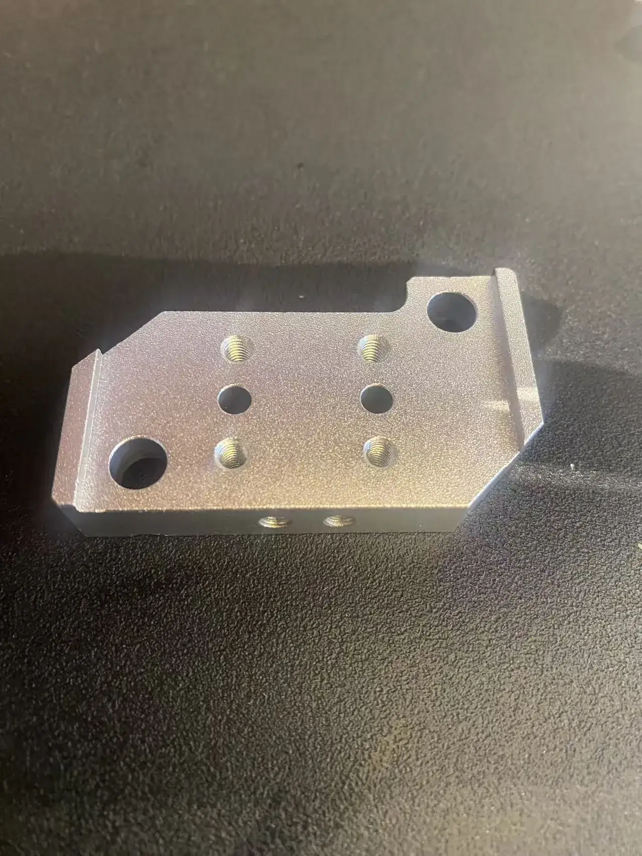 Aluminium mounting plate seen from above with four tapped holes, two through holes, two larger corner holes and two tapped holes in the long side face