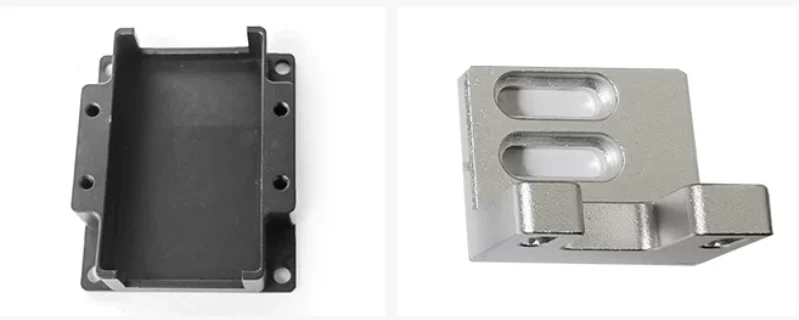 A black anodised aluminium enclosure body hollowed out of a solid block with integral mounting lugs, beside a natural finish milled block with two obround recesses