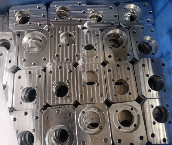 A crate of identical machined aluminium bodies, each with a stepped bore, a counterbored seal face and a bolt circle