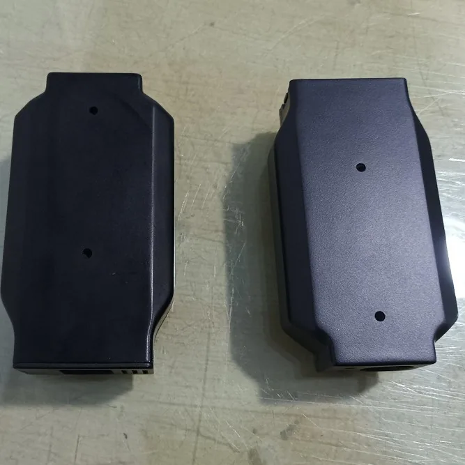 Two black plastic housings with small holes on the top face, side by side on a scratched grey surface
