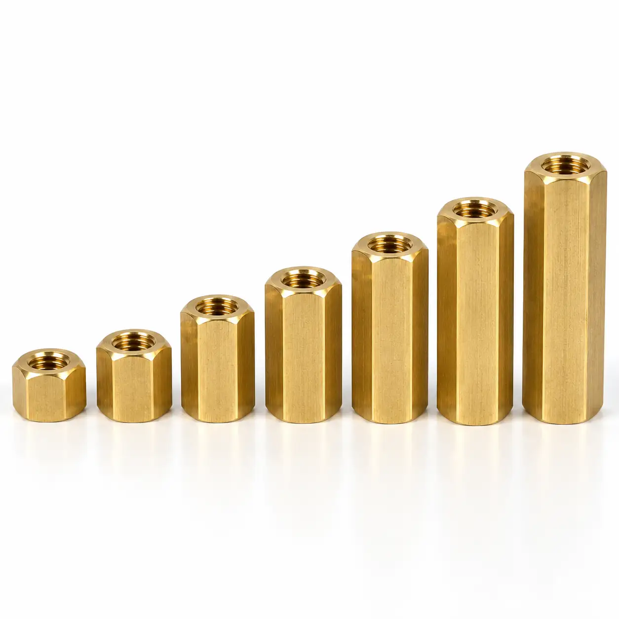 Seven brass hex coupling nuts standing on end in a rising series on a white background, the across-flats and the body length both stepping up from the short nut on the left to the long one on the right, with the tapped through hole visible down the bore of each