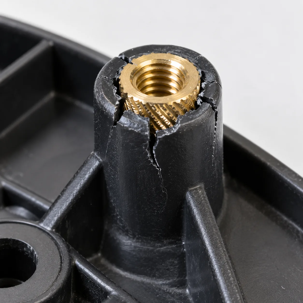 A black plastic boss split by two cracks running down its wall, the brass insert still seated in it