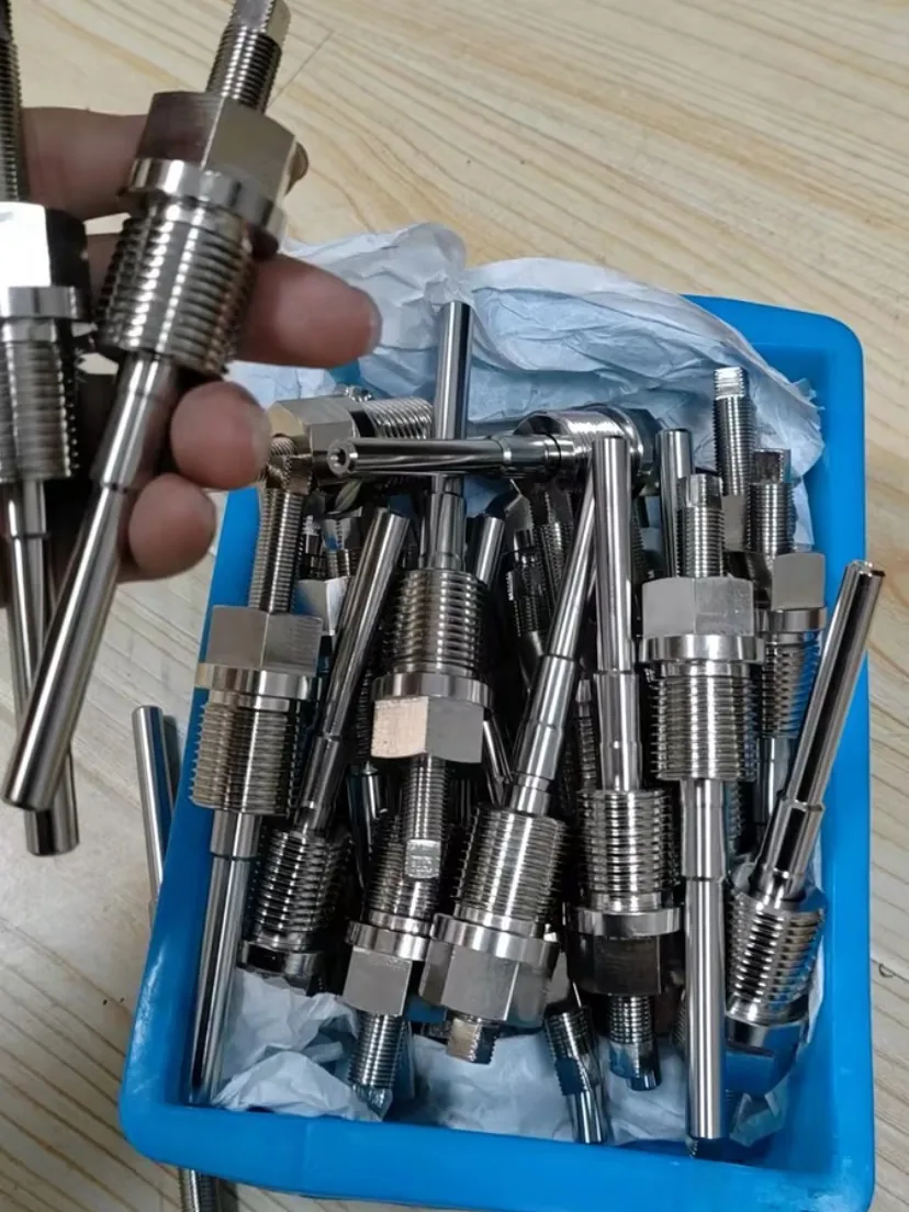 Box of machined threaded thermowells with hex, male process thread and long stepped stems, one held in hand
