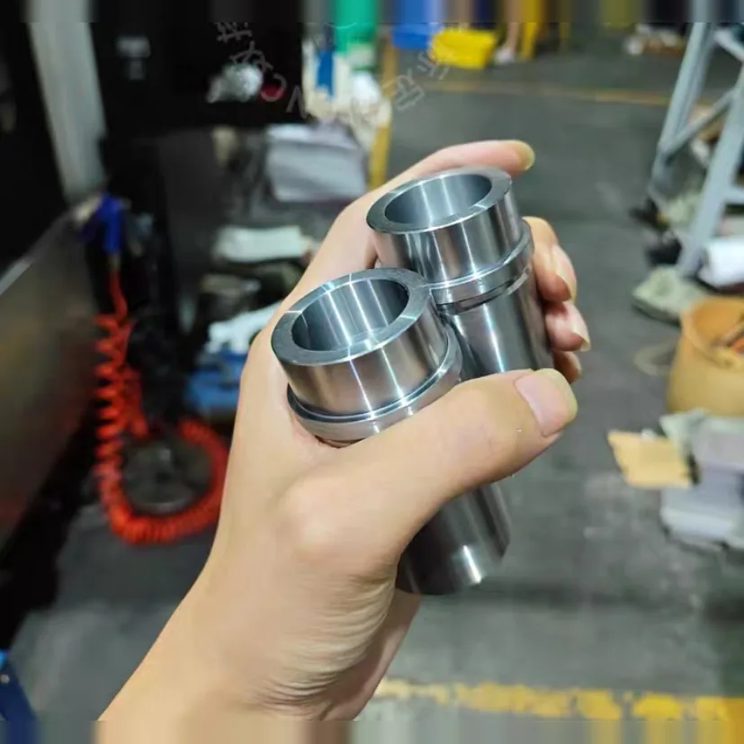 Hand holding two bored steel sleeves with a collar and an outside groove, in a workshop