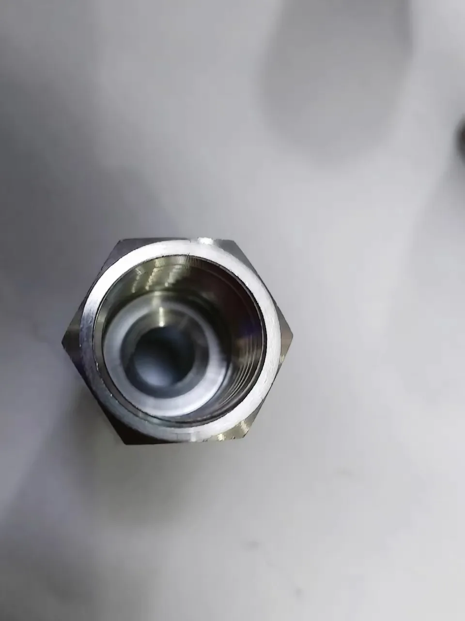 End view into the female thread of a machined stainless gauge adapter showing clean internal threads and hex body