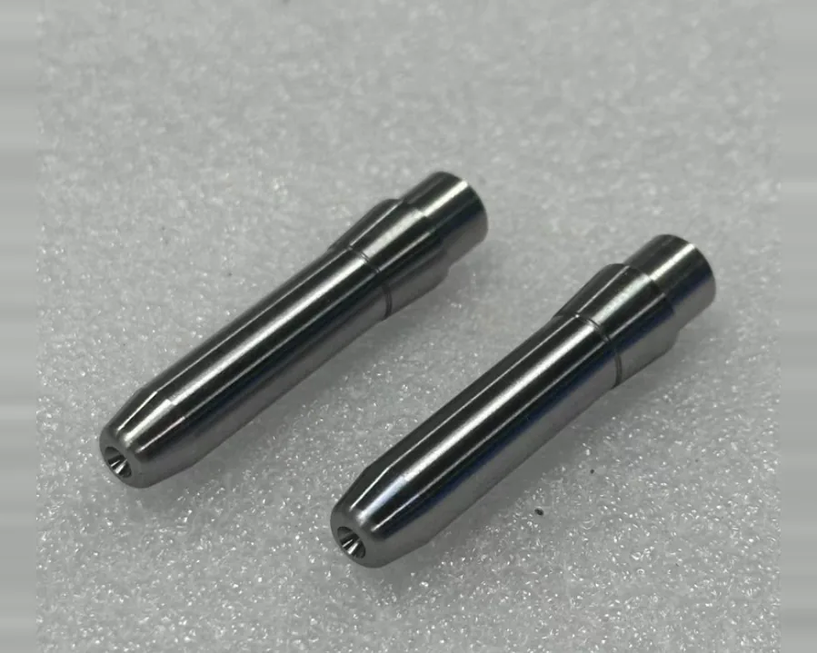 Two turned metal pins with a stepped body and a tapered tip with a small central bore, on a grey surface