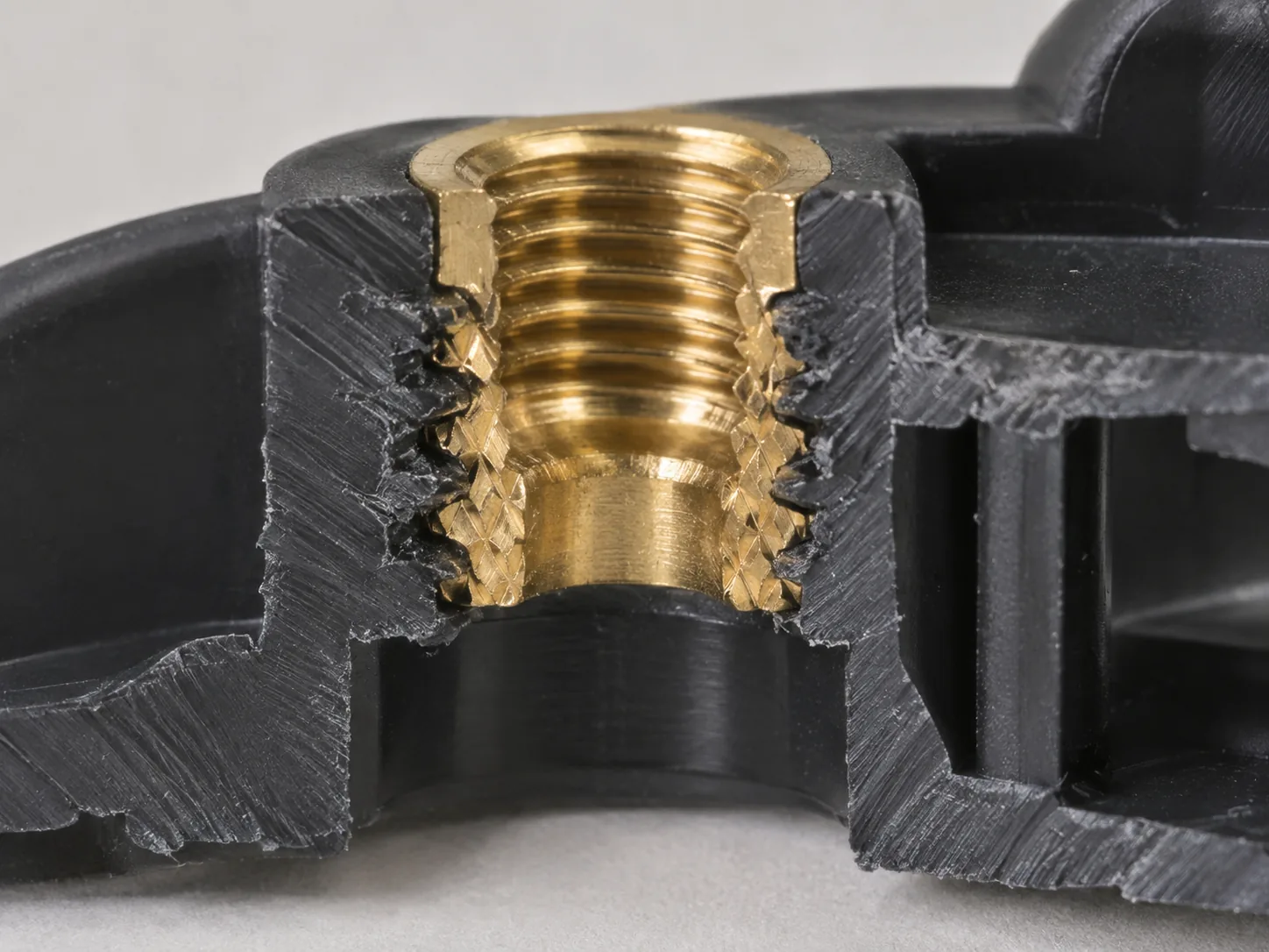 Sectioned black plastic housing with a brass insert moulded into the boss: two diamond-knurl bands with a plain waist between them, plastic keyed into the knurl on both sides, internal thread visible