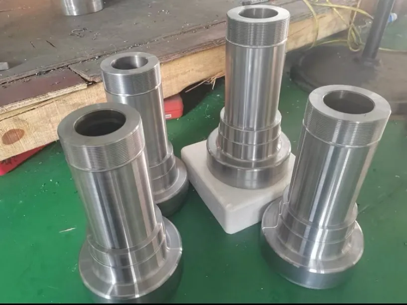 Four large turned sleeves standing on a green floor, each with a flanged base and an external thread at the top