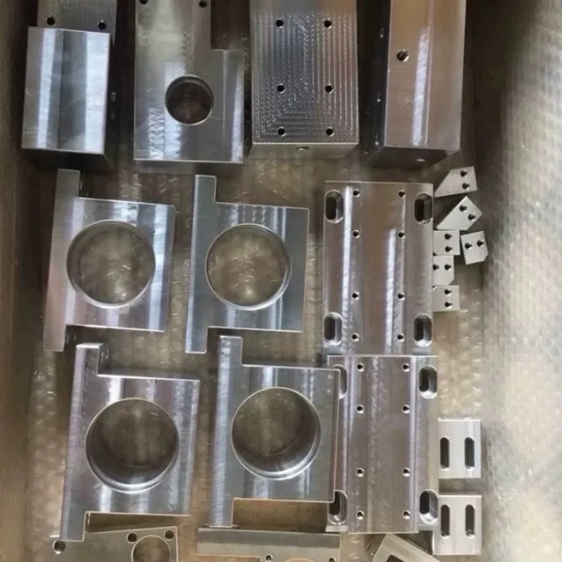 Box of milled metal parts: blocks with a large round bore, slotted plates and small locator plates