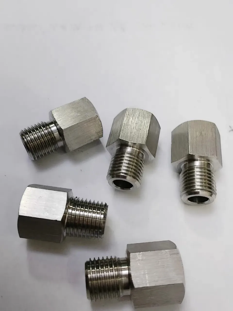 Five freshly machined stainless steel female to male pressure gauge thread adapters on a workshop bench