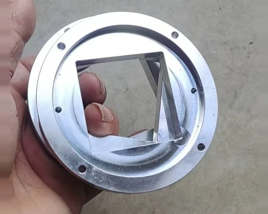 Hand holding a machined round flange with a bolt circle of holes and a square opening cut through the centre