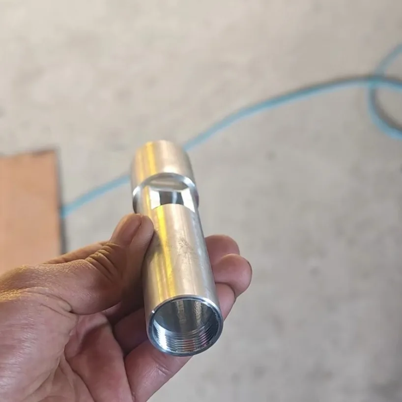 Machined metal tube with a rectangular window slot near one end and an internal thread at the open end