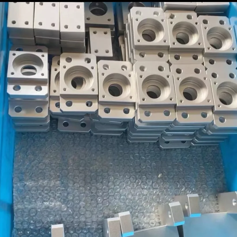 Crate of machined square flange blocks, each with a counterbored centre bore and four corner holes