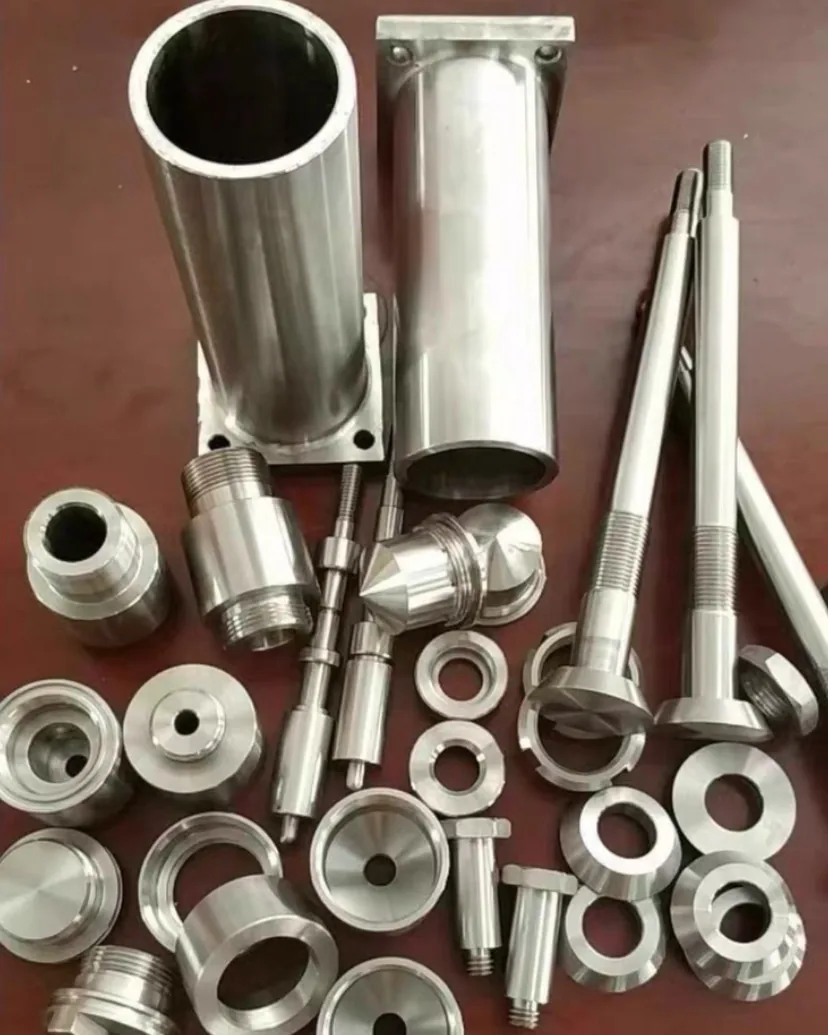 Turned process parts on a table: tubes with square flanges, threaded bodies, conical seats, rings and long stems with disc heads