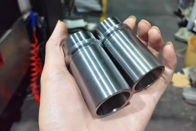 Two turned steel sleeves held in hand, each with an outside groove near one end and a bored inside