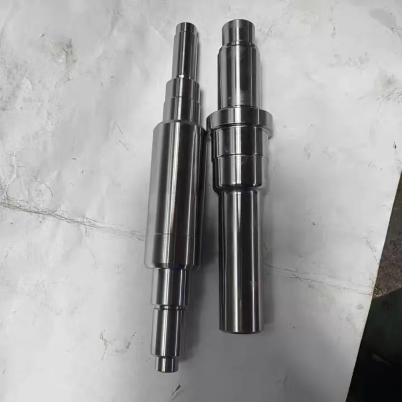Two turned stepped steel shafts on white paper, one with a collar near its middle