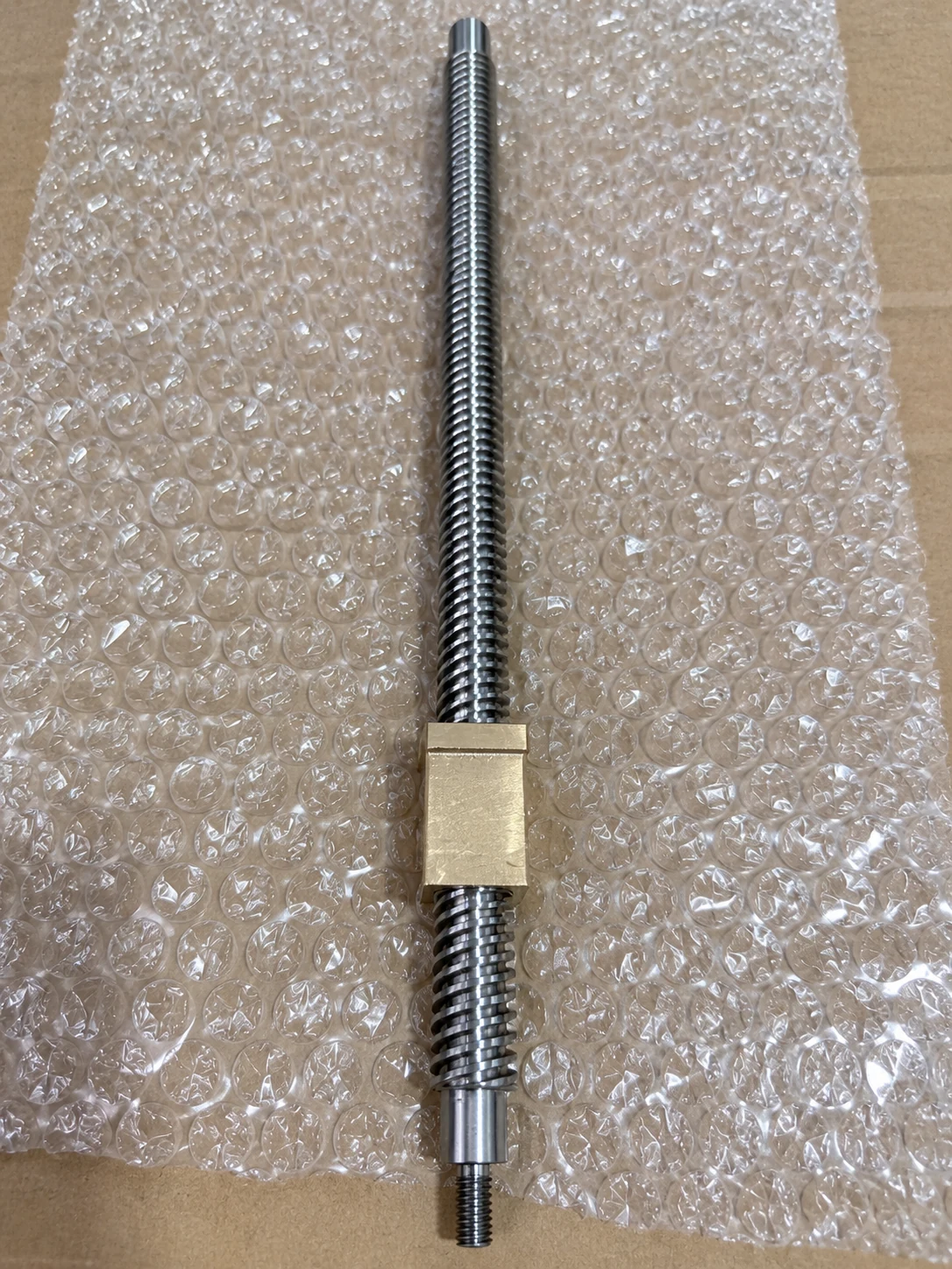 Trapezoidal lead screw with a bronze block nut, a short plain journal at one end and a small metric thread at the other, on packing foam