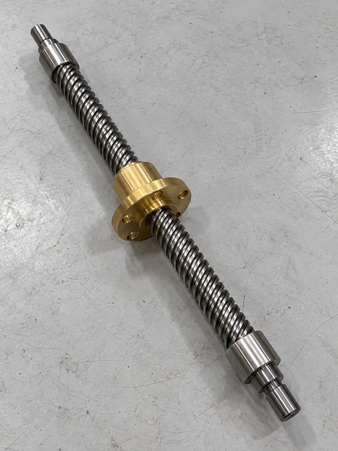 Trapezoidal lead screw made by EKINSUN with a bronze round flange nut, four mounting holes on the flange, both ends turned down to stepped plain journals