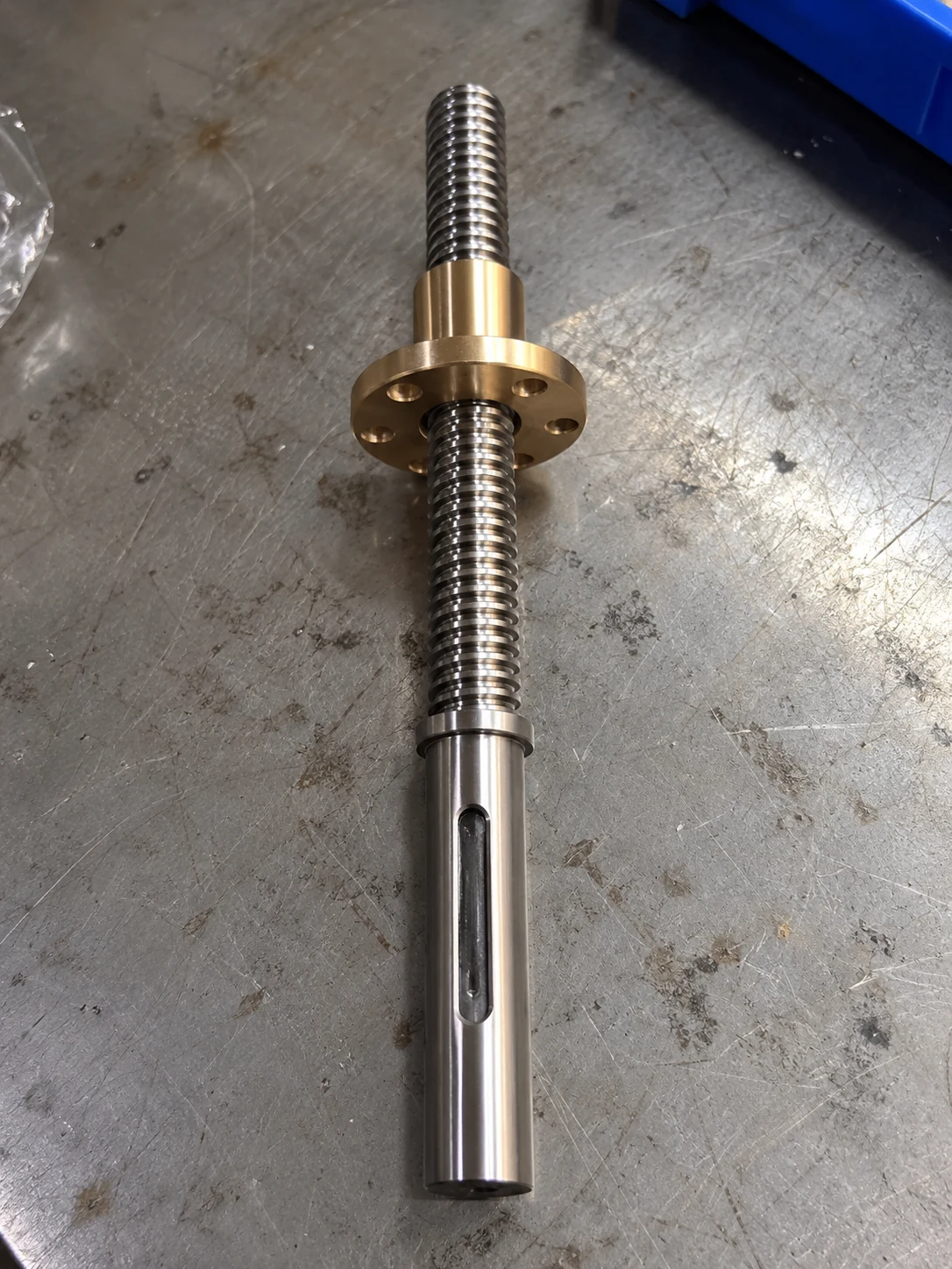 Trapezoidal lead screw with a bronze flange nut and a plain shaft end carrying a keyway and a shoulder