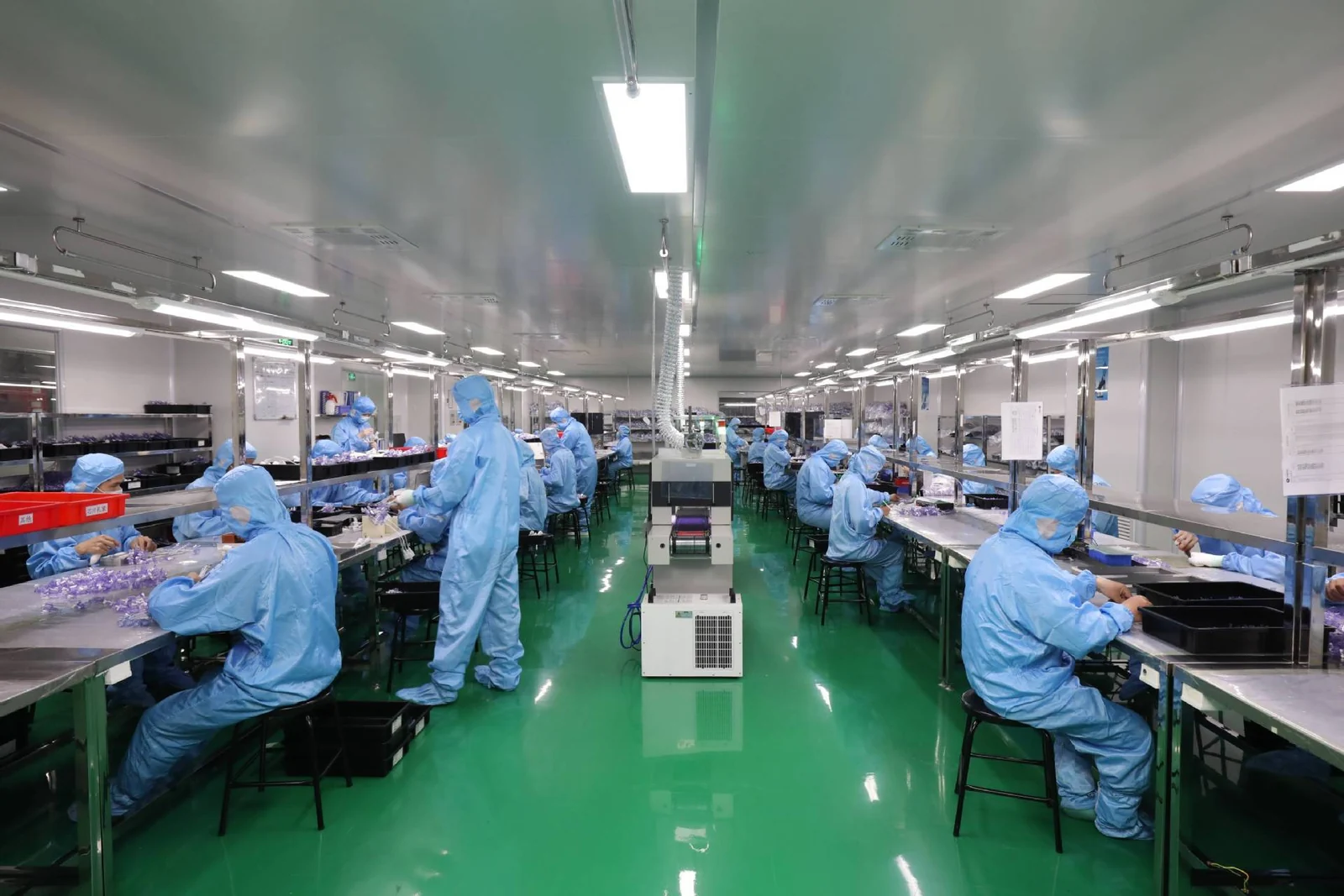 Class 100,000 cleanroom assembly hall at the ISO 13485 medical molding facility with gowned and hooded operators at stainless benches under HEPA-filtered ceiling supply