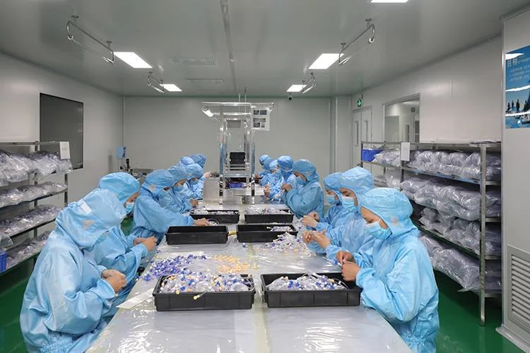 Operators in cleanroom gowns assembling small blue and clear medical connector components at a central stainless bench