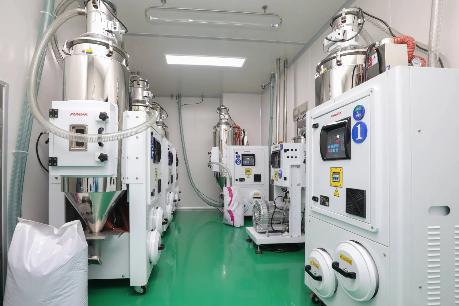 Resin drying room at the ISO 13485 medical molding facility: stainless dehumidifying hopper dryers with numbered control stations and sealed material transfer lines