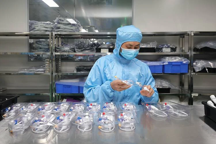 Cleanroom operator inspecting finished high-pressure manifold and stopcock sets with colour-coded Luer fittings laid out in blister trays