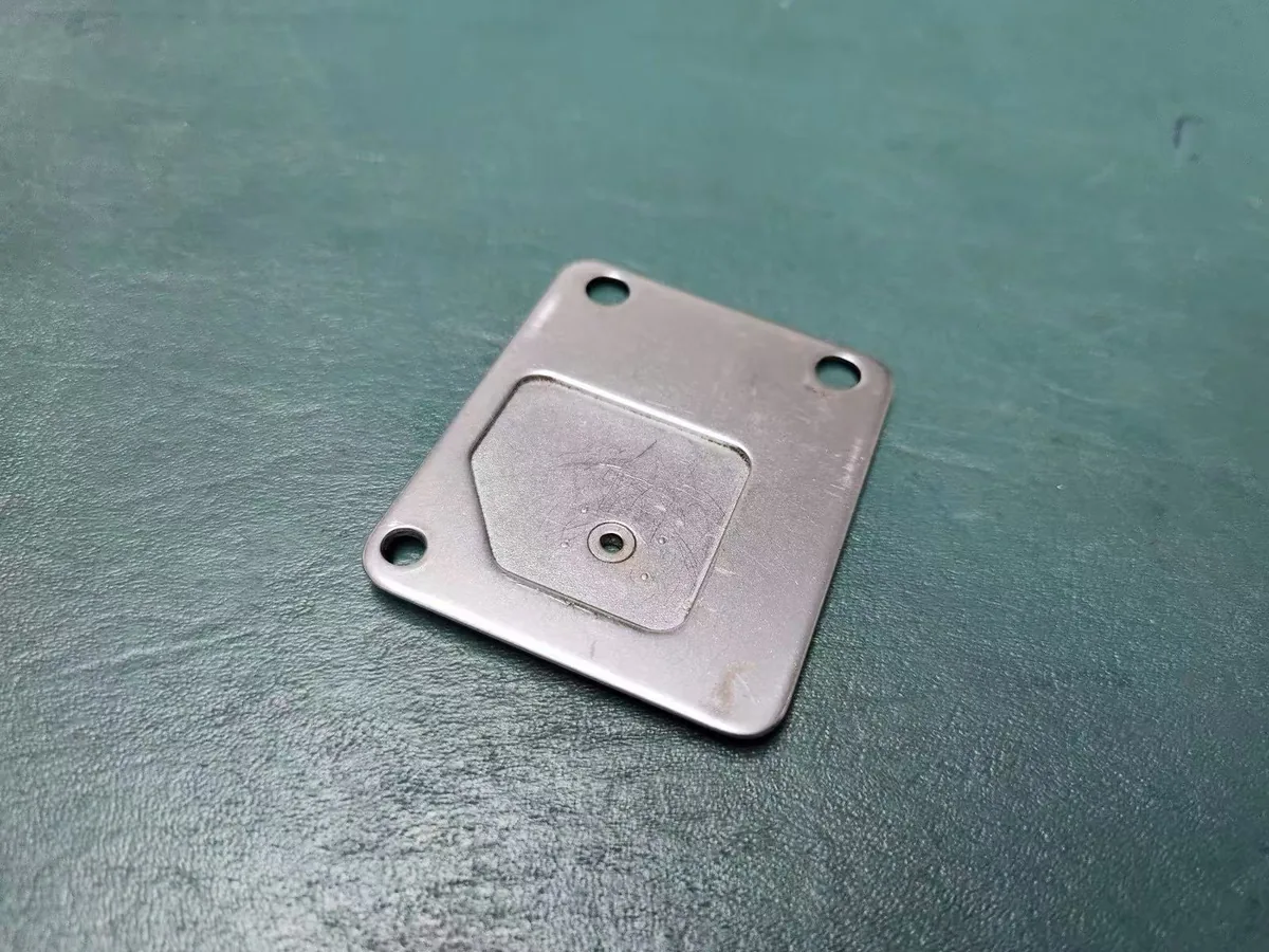 Underside of an embroidery machine needle plate showing the polygonal pad joined into the main plate at the factory, with the countersunk needle hole at its centre