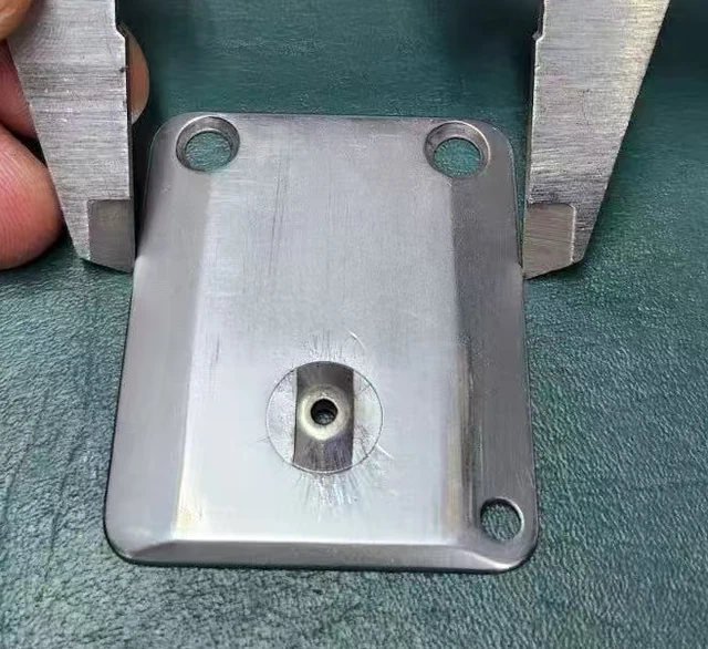 Worn embroidery machine needle plate sent in by a customer, showing radial thread scoring fanning out from an enlarged needle hole in the raised strip
