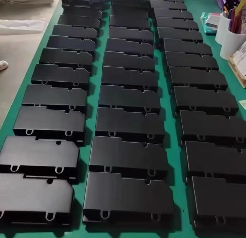 Around thirty identical black vacuum cast plastic cover plates arranged in rows on a green workbench