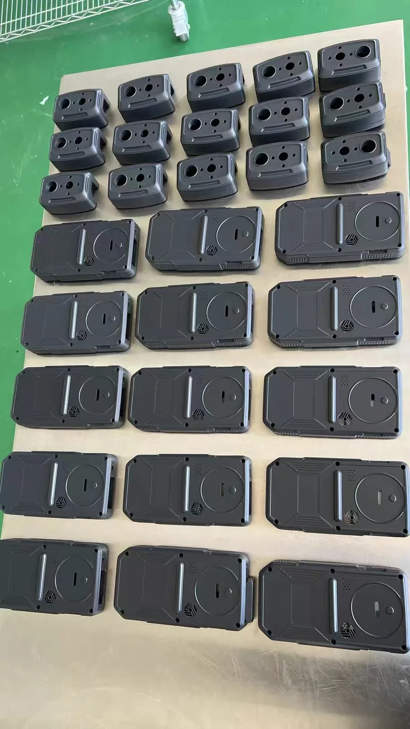 Batch of around 35 vacuum cast grey and black plastic enclosure bodies and back covers laid out on a workbench
